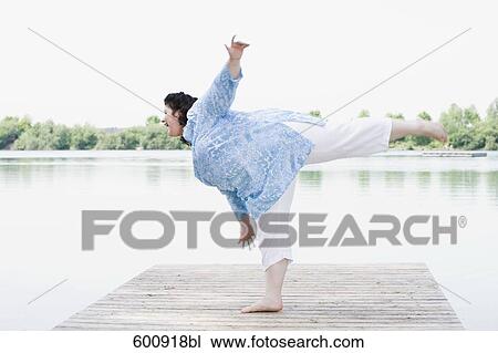 Stock Image - overweight woman doing stretching exercises on pier by lake. Fotosearch