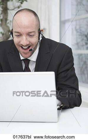 portrait of businessman wearing headset working with laptop computer View Large Photo Image Stock Image - portrait of businessman wearing headset working with laptop computer. Fotosearch