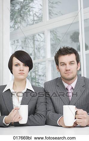 Stock Image - portrait of two business people sitting at table with cups. Fotosearch