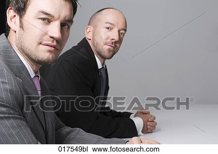 Stock Image - portrait of two businessmen sitting at conference table. Fotosearch
