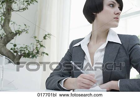 Stock Image - portrait of young businesswoman sitting at desk taking notes. Fotosearch