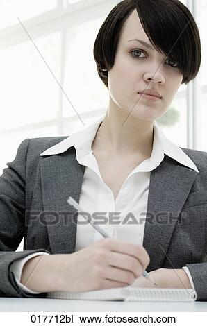 Stock Image - portrait of young businesswoman sitting at desk taking notes. Fotosearch