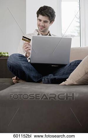 portrait of young man sitting on sofa with laptop computer holding credit card View Large Photo Image Stock Image - portrait of young man sitting on sofa with laptop computer holding credit card. Fotosearch