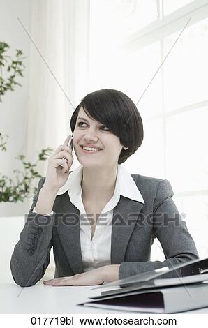 portrait of young woman sitting at desk and talking on mobile phone View Large Photo Image Stock Image - portrait of young woman sitting at desk and talking on mobile phone. Fotosearch