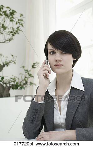 portrait of young woman sitting at desk and talking on mobile phone View Large Photo Image Stock Image - portrait of young woman sitting at desk and talking on mobile phone. Fotosearch