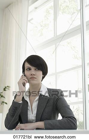 portrait of young woman sitting at desk and talking on mobile phone View Large Photo Image Stock Image - portrait of young woman sitting at desk and talking on mobile phone. Fotosearch