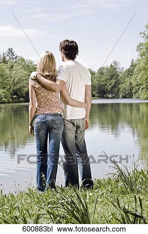 Stock Image - rear view of young couple standing by lake. Fotosearch