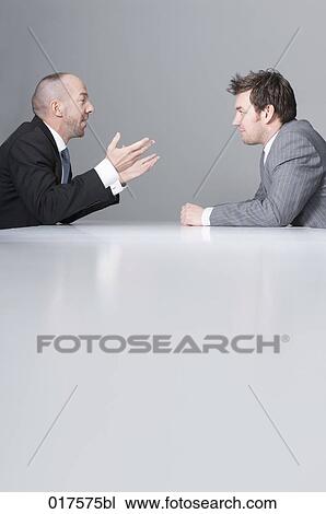 Stock Image - two businessmen sitting at conference table. Fotosearch