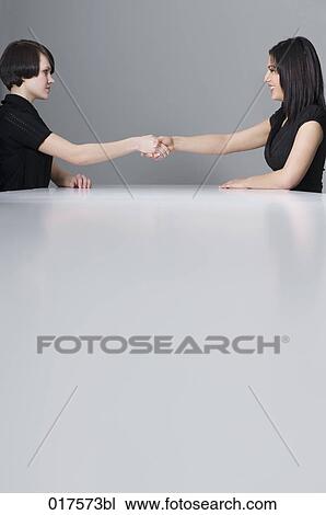 Stock Image - two businesswomen shaking hands at conference table. Fotosearch
