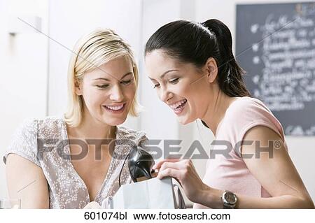Stock Image - two female friends at restaurant looking at shoe in shopping bag. Fotosearch
