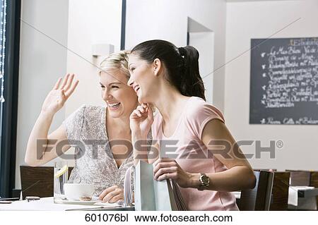 Stock Image - two female friends sitting in restaurant looking out of window. Fotosearch