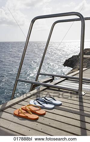 Stock Image - two pairs of flip flops on pier. Fotosearch