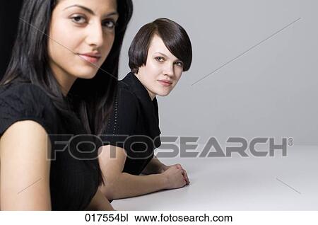two young businesswomen sitting at conference table View Large Photo Image Stock Image - two young businesswomen sitting at conference table. Fotosearch