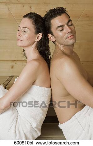 Stock Image - woman and man relaxing in sauna sitting back to back. Fotosearch