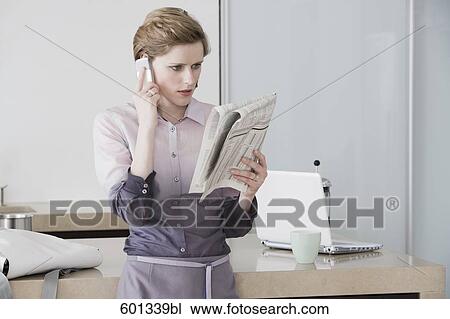 woman at morning standing in kitchen reading newspaper and talking on mobile phone View Large Photo Image Stock Image - woman at morning standing in kitchen reading newspaper and talking on mobile phone. Fotosearch
