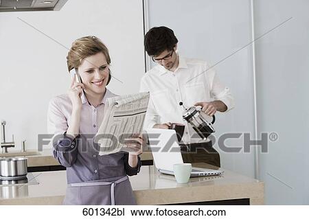 woman at morning standing in kitchen reading newspaper while man is making coffee View Large Photo Image Stock Image - woman at morning standing in kitchen reading newspaper while man is making coffee. Fotosearch