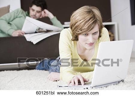 Stock Image - woman working with laptop computer at home while man is reading newspaper. Fotosearch