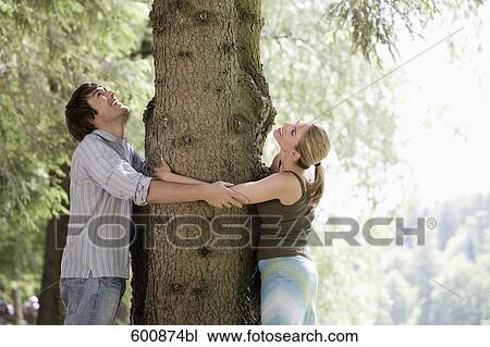 Stock Image - young couple in park embracing tree. Fotosearch