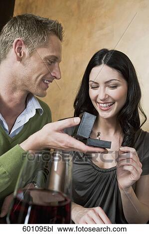 Stock Image - young couple sitting at restaurant man giving woman ring. Fotosearch