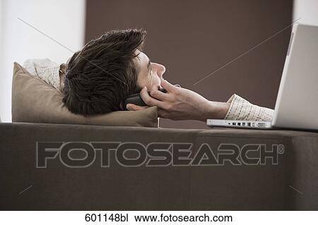 young man reclining on sofa and talking on mobile phone View Large Photo Image Stock Image - young man reclining on sofa and talking on mobile phone. Fotosearch