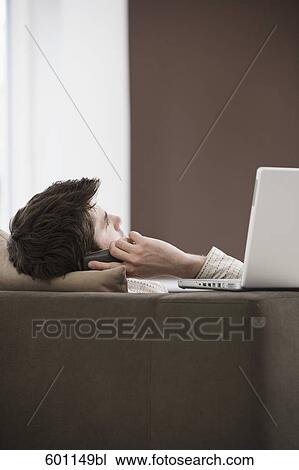 young man reclining on sofa and talking on mobile phone View Large Photo Image Stock Image - young man reclining on sofa and talking on mobile phone. Fotosearch