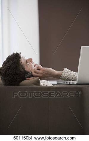 young man reclining on sofa and talking on mobile phone View Large Photo Image Stock Image - young man reclining on sofa and talking on mobile phone. Fotosearch