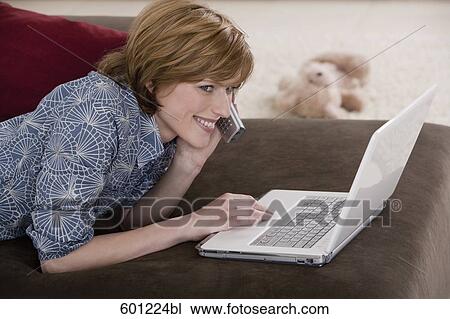 Stock Image - young woman at home working with laptop computer and talking on telephone. Fotosearch