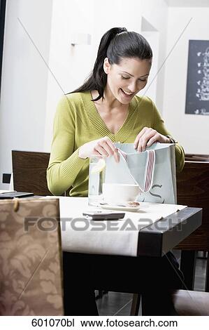 young woman sitting at restaurant table looking in her shopping bag View Large Photo Image Stock Image - young woman sitting at restaurant table looking in her shopping bag. Fotosearch