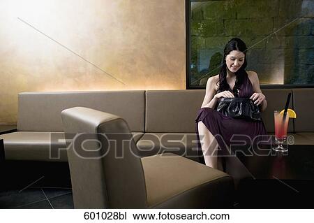 young woman sitting in bar looking for something in her handbag View Large Photo Image Stock Image - young woman sitting in bar looking for something in her handbag. Fotosearch