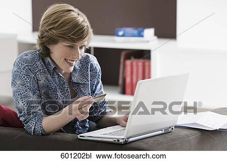 Stock Image - young woman with laptop computer at home holding credit card. Fotosearch