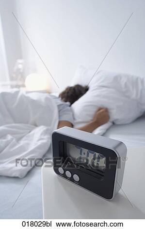 Stock Image - alarm clock on sideboard with woman sleeping in bed. Fotosearch