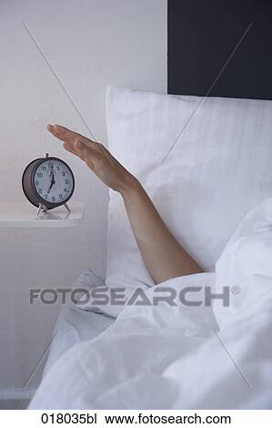 Stock Image - arm of sleeping woman switching off alarm clock. Fotosearch