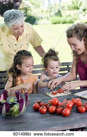 Stock Image - family preparing salad of tomatoes in garden. Fotosearch