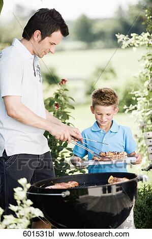 Stock Image - father and son grilling together at barbecue. Fotosearch