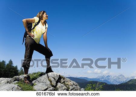Stock Image - full body portrait of mature woman standing on rock in the mountains. Fotosearch