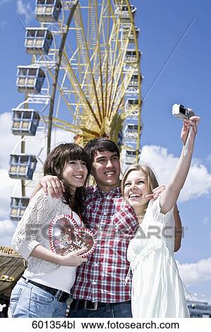 group of three friends at fun fair taking photo of themselves View Large Photo Image Stock Image - group of three friends at fun fair taking photo of themselves. Fotosearch