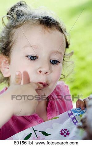 Stock Image - headshot of little girl tasting cake with finger. Fotosearch