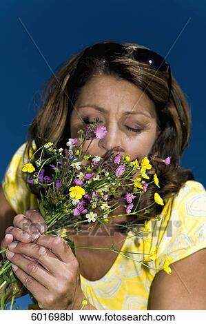 Stock Image - headshot of mature woman smelling summer flowers. Fotosearch