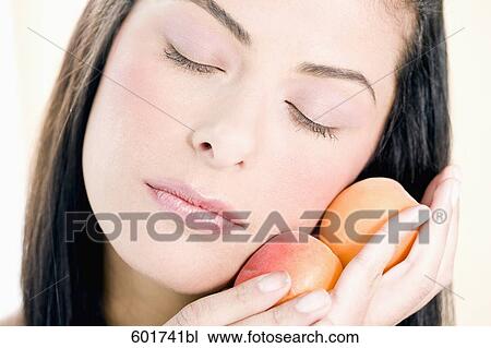 headshot of young woman holding peaches against her cheek View Large Photo Image Stock Image - headshot of young woman holding peaches against her cheek. Fotosearch