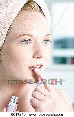 Stock Image - headshot of young woman putting lipstick with finger on mouth. Fotosearch