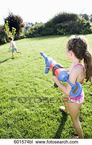 Stock Image - little girl chasing her sister in garden with water pistol. Fotosearch