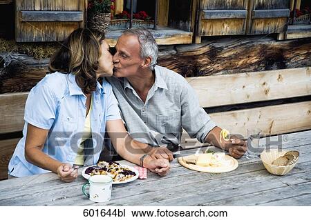 Stock Image - mature couple kissing during meal in front of alpine hut. Fotosearch