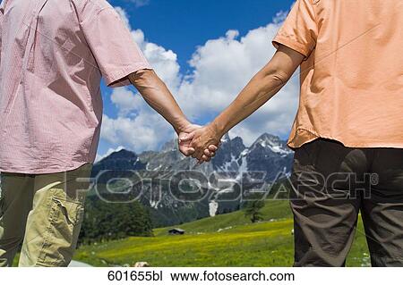 mature couple standing in front of mountains holding hands View Large Photo Image Stock Image - mature couple standing in front of mountains holding hands. Fotosearch