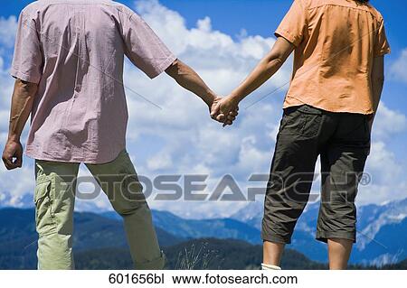 Stock Image - mature couple standing in front of mountains holding hands. Fotosearch