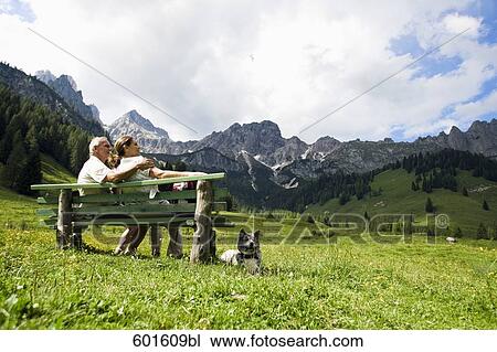 mature couple with dog sitting on bench in front of mountains View Large Photo Image Stock Image - mature couple with dog sitting on bench in front of mountains. Fotosearch