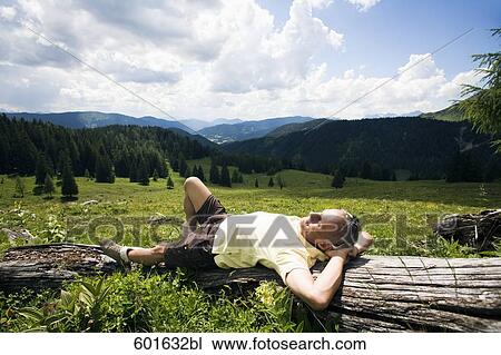 Stock Image - mature man dozing on log in the mountains. Fotosearch