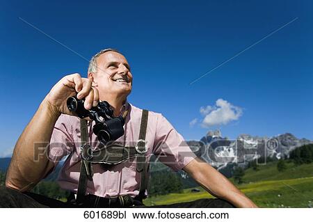 Stock Image - mature man in the mountains holding binoculars. Fotosearch
