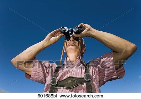 Stock Image - mature man in the mountains looking through binoculars. Fotosearch