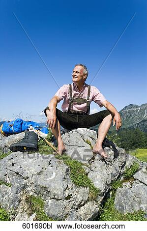 Stock Image - mature man sitting barefoot on rock in the mountains. Fotosearch