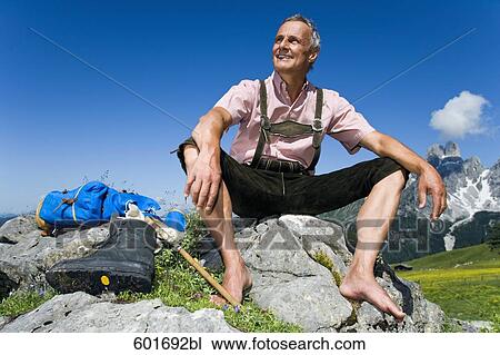 Stock Image - mature man sitting barefoot on rock in the mountains. Fotosearch